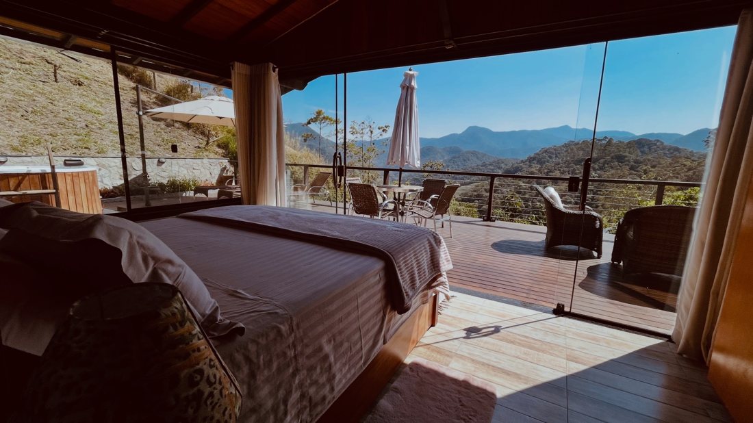 Quarto do chalé com porta de vidro aberta para o deck e as montanhas