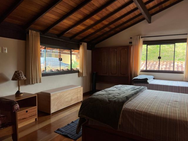Quarto com cama de casal e solteiro sob o telhado de madeira
